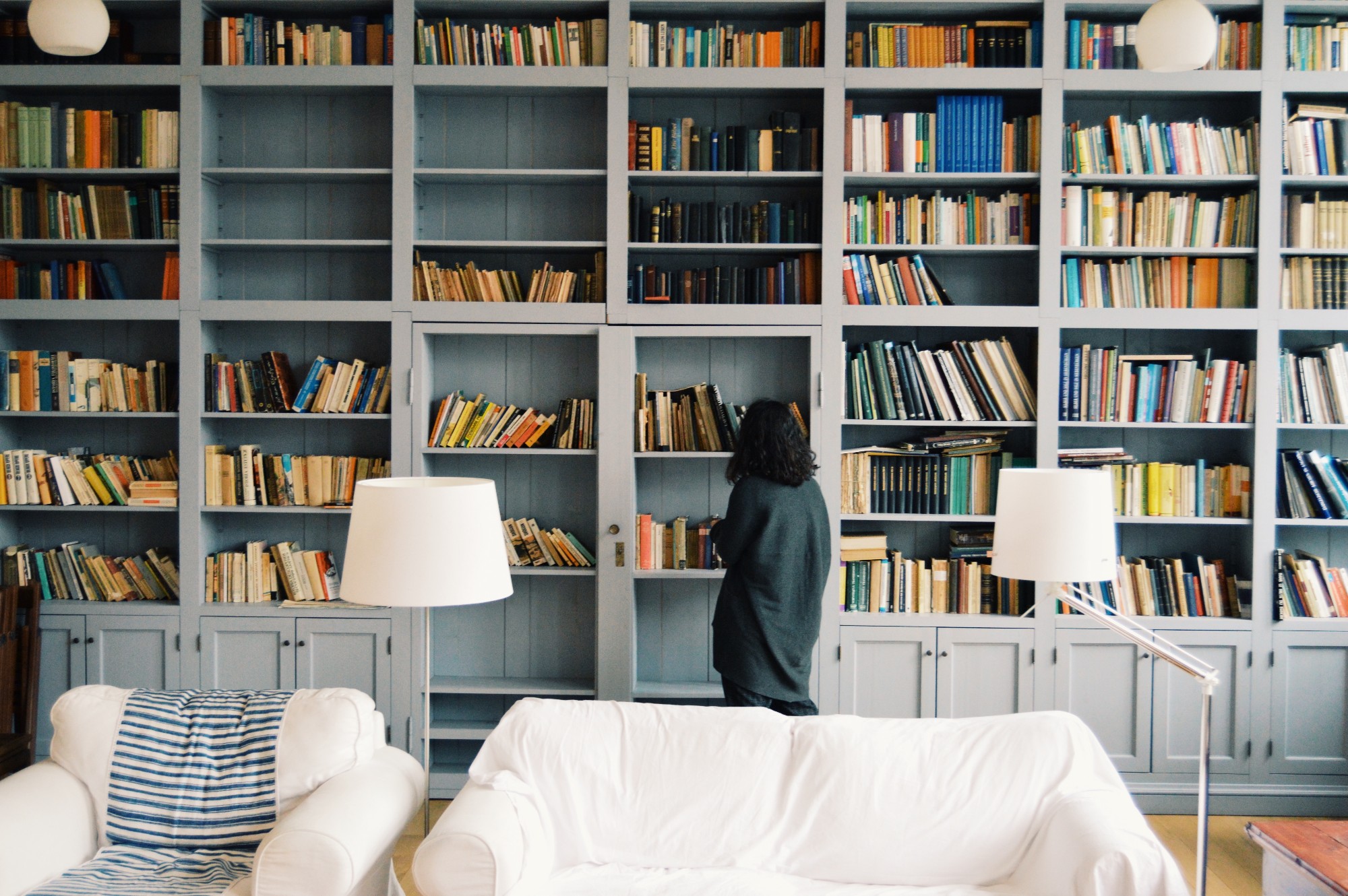 Woman choosing book of large living room shelves, Photo by Radu Marcusu on Unsplash